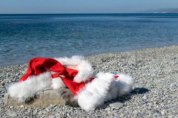 Santa Claus clothing and hat lies on a large stone on the seashore. Santa went swimming