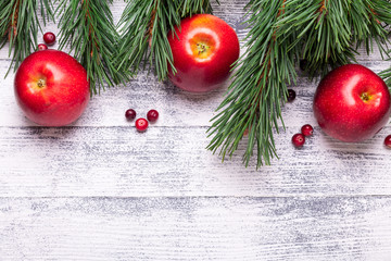 Christmas background with tree branches, red apples and cranberries. Light wooden table. Top view. Copy space