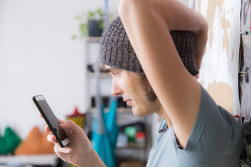 Young man with hat using smartphone at home