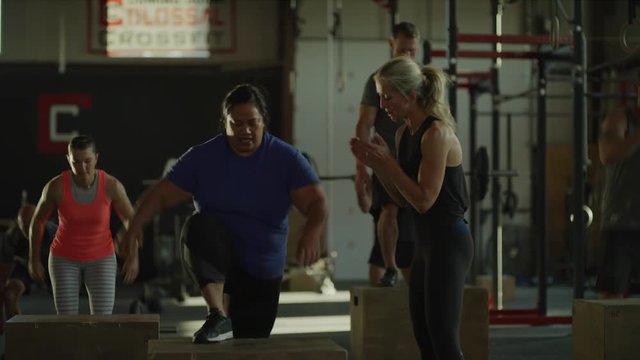 Slow motion shot of fitness instructor congratulating woman for successful box jump in gymnasium / Lehi, Utah, United States
