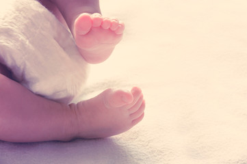 Legs of a newborn baby lying on the bed. Tinted and blur. Selective focus.