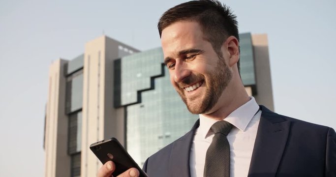 Confident multiethnic in suit and tie businessman texting on his smartphone via internet in the street - closeup 4k