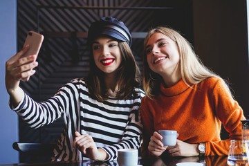 Two young women sitting in a cafe, drinking their morning coffee and surfing the net on smart phones.