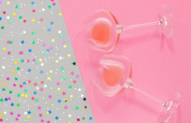 top view on glasses with champagne on a gray-pink background with festive confetti from multi-colored stars. Festive holiday background. Celebration concept. Flat lay