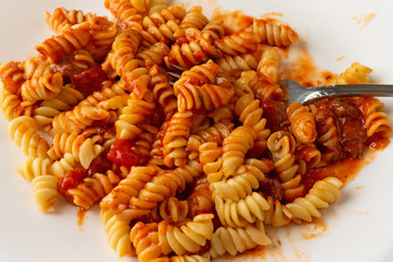 Close view of a portion of rotini pasta in a sausage and tomato sauce on a plate with a fork.