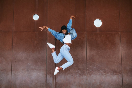 Cool woman wearing denim clothes dancing outdoors.