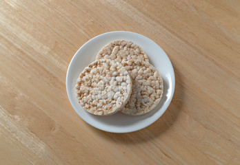 Top view of three multigrain rice cakes on a white plate atop a wood table.