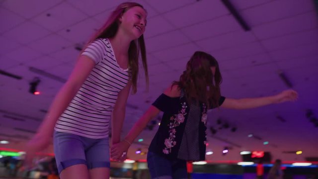 Slow motion tracking shot of girls skating and laughing at roller skating rink / Orem, Utah, United States