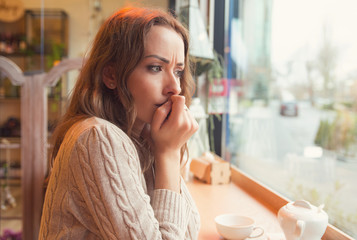 Nervous woman biting nails and looking away sitting alone in a coffee shop