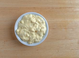 Top view of a portion of potato and egg salad in a small bowl on a wood table.