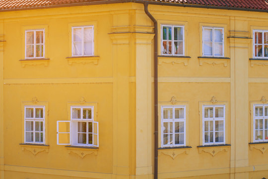 Windows with white frames on the yellow facade of the building in Europe. Reflection in the Windows of the house orange in the Czech Republic. Drainpipe on the corner of the yellow building.