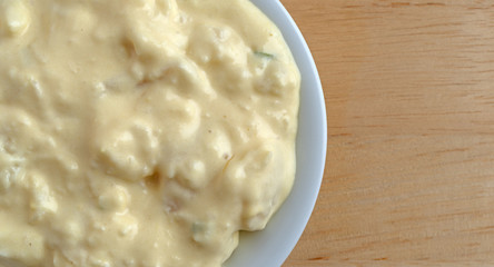 Top close view of a portion of potato and egg salad in a small bowl on a wood table.