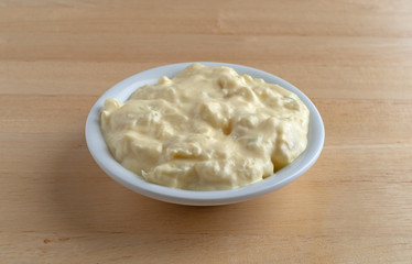Side view of a portion of potato and egg salad in a small bowl on a wood table.