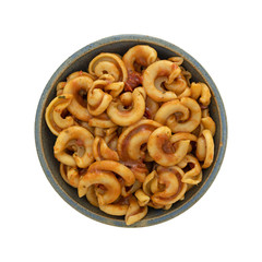 Overhead view of cold pasta with tomato chunks and seasonings with olive oil in an old stoneware bowl isolated on a white background.