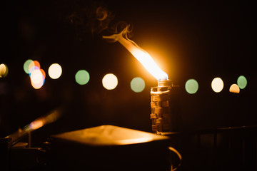 Close-up of burning Tiki torch at night with colourful bokeh in the background