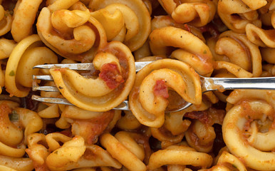 Top close view of cold pasta with tomato chunks and seasonings with olive oil with a fork in the food.