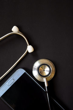 Medical conceptual image with the view of stethoscope and smartphone, on the black background.