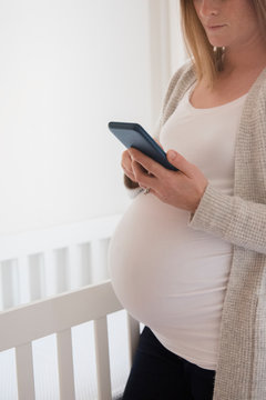 Pregnant woman texting next to crib