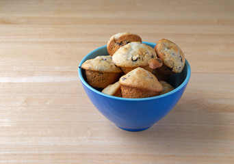 Several freshly baked bite size blueberry muffins filling a blue bowl on a wood table.