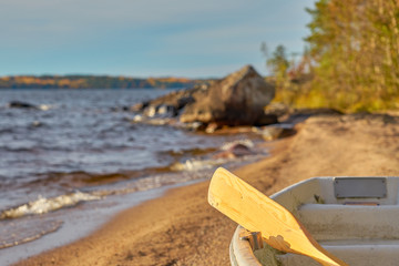                              A wooden paddle  on a boat on a sandy beach with a blurred lake shore on a background.