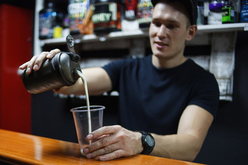 young male athlete making a protein shake. pours it into a glass