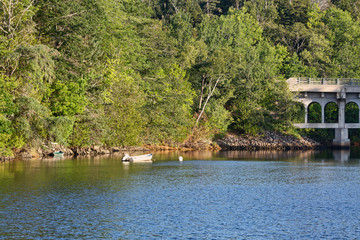 A moored skiff and another tied to the bank of a tidal river with a bridge in the background on the coast of Maine in the summertime.