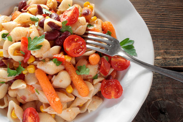 Vegetarian vegetable pasta. Pasta shells with tomato, baby carrot, paprika, beans, sweet corn and chickpea on wooden background. Top view.