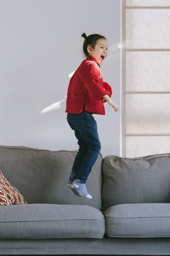Lovely little girl in chinese custom holding a latern and jumping on sofa