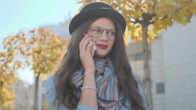 Portrait of beautiful girl wearing hat talking on smartphone outdoor. Conversation on mobile phone.