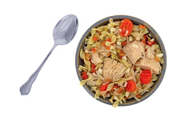 Top view of a home made chicken noodle soup in an old stoneware bowl with a spoon to the side isolated on a white background.