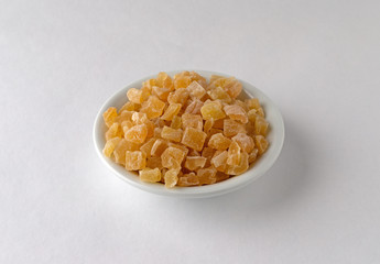 A small bowl filled with dried diced peaches on a white background illuminated with window light.