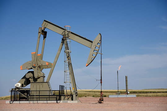 Crude oil pump jack with natural gas flaring and a clear blue sky, Powder River Basin, Wyoming