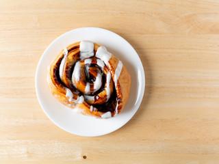 Top view of a freshly baked cinnamon roll on white plate atop a wood table.