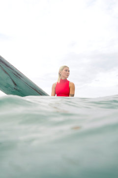 Young woman sits on the surfboard in the ocean, underwater splitted shot.