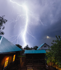 Thunderbolt in the night sky over the village with houses and garden