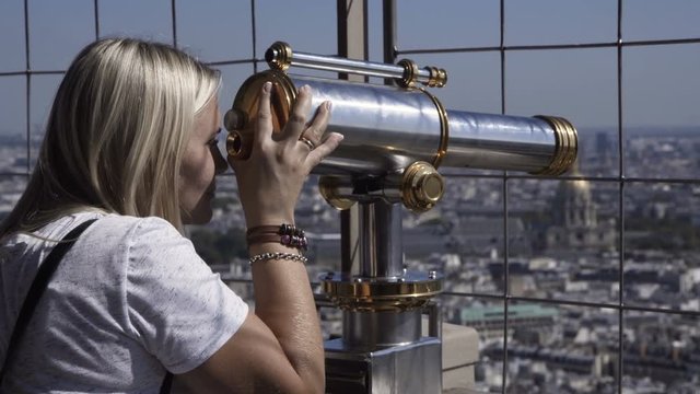 Woman on viewpoint of Eiffel tower looking at cityscape through coin binocular, Paris