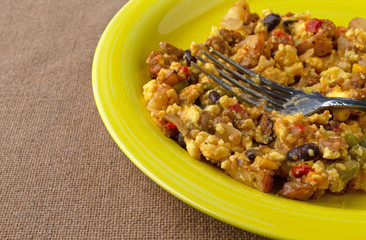 A scrambled egg burrito meal on a yellow plate with a fork atop a brown tablecloth.