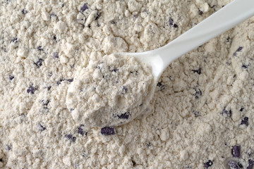 Top view of a white plastic spoon with a spoonful of clumpy blueberry muffin mix with imitation blueberries.