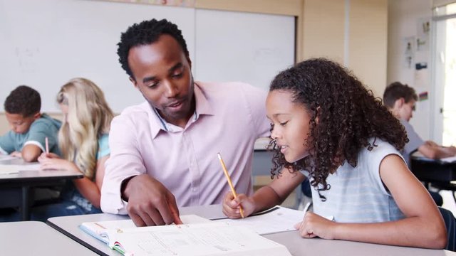 Male elementary school teacher working in class with girl
