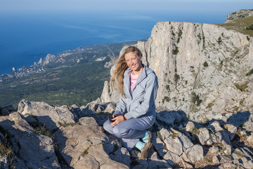 Naklejka na ściany i meble girl sitting on top of a mountain overlooking the sea and the city and smiling