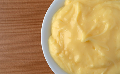 Top close view of homemade banana cream pudding in a white dish atop a wood table illuminated with window light.