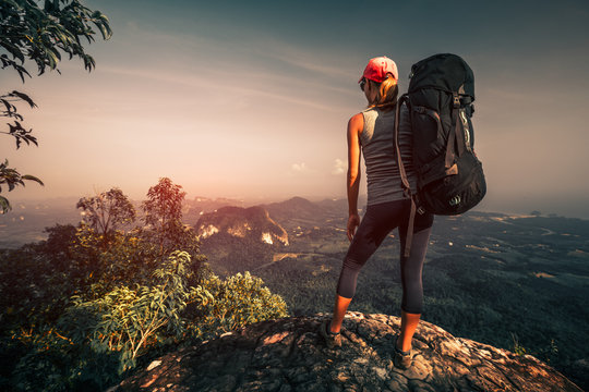 Young woman with backpack stands on top of the mountain - Powered by Adobe