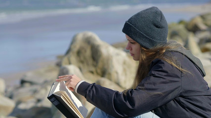 Obraz premium Young woman sits at the ocean while reading a book