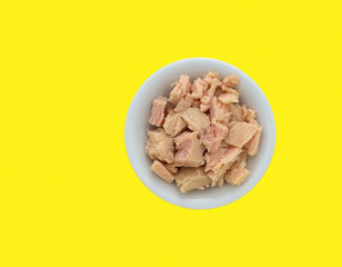 Top view of a bowl filled with solid white albacore tuna in olive oil chunks on a bright yellow background.