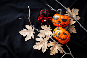 Halloween concept background of funny pumpkin and red spider on paper leaves over blurred black fabric texture background