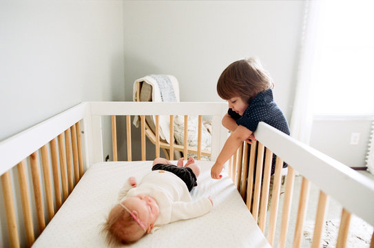 brother looks in on little baby sister in her crib