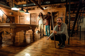 A group of male friends smile and pose by a pool table in a cabin in upstate New York
