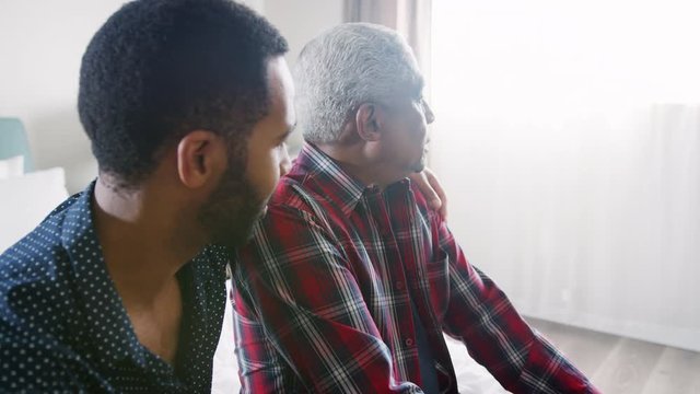 Adult Son Comforting Senior Father Suffering With Depression At Home