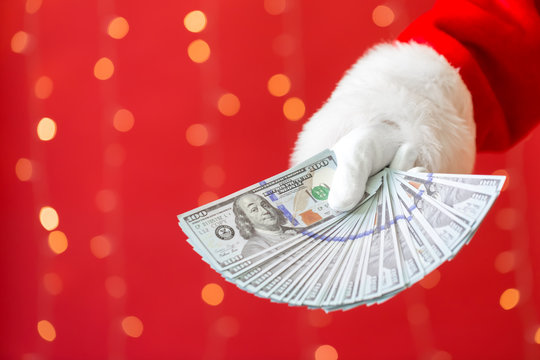 Santa holding US dollar bills on a shiny light red background