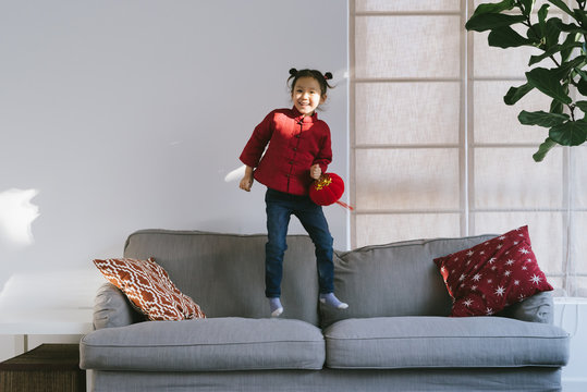 Lovely little girl in chinese custom holding a latern and jumping on sofa
